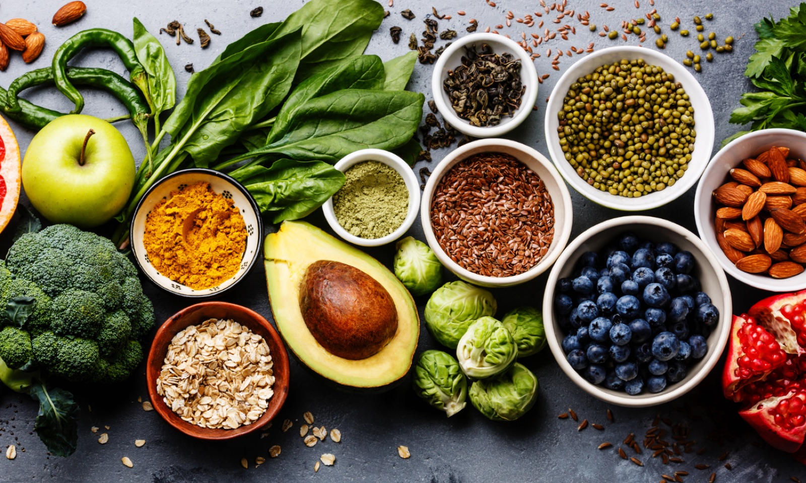 Bowls of blueberries, almonds, lentils and turmeric with avocado, broccoli and spinach