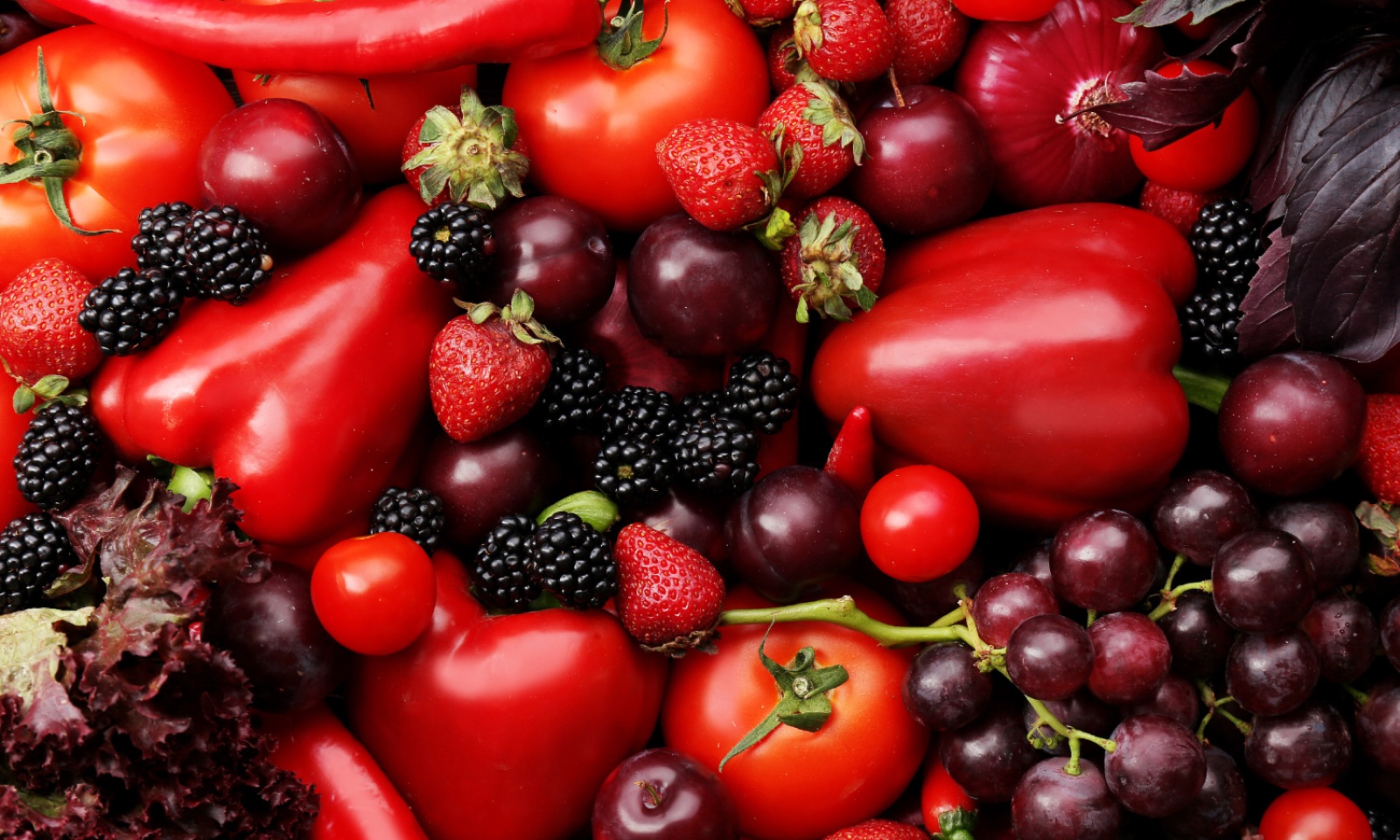 Red peppers, tomatoes, strawberries, blackberries and plums piled together